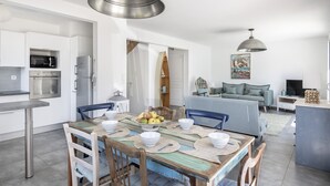 A modern kitchen with stainless steel appliances, a dining area with a wooden table and blue chairs, and a living room with a grey sofa and a painting on the wall. - 100m from the beach, house for 7, seaview (Baden)