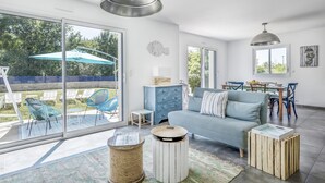 A spacious living room with a large sliding glass door leading to a patio area, a blue sofa, and a dining table with chairs. - 100m from the beach, house for 7, seaview (Baden)