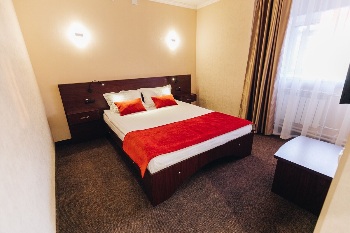 A hotel room with a bed, bedside tables, a desk, and a window with curtains.