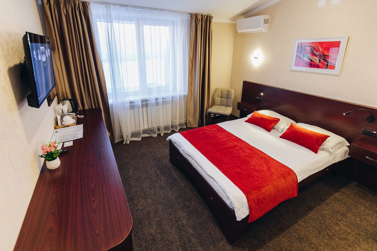A hotel room with a bed, a desk with a computer, a chair, and a TV.