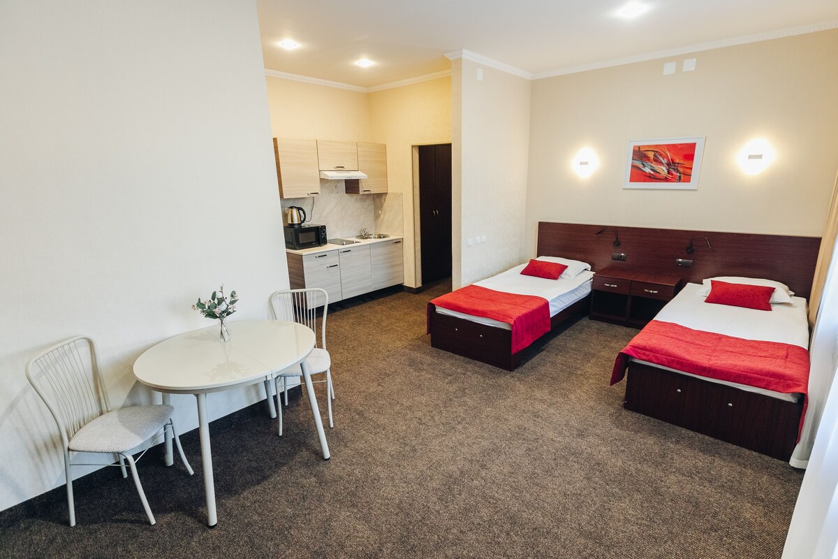 A compact hotel room with a single bed, a small desk, and a kitchenette.
