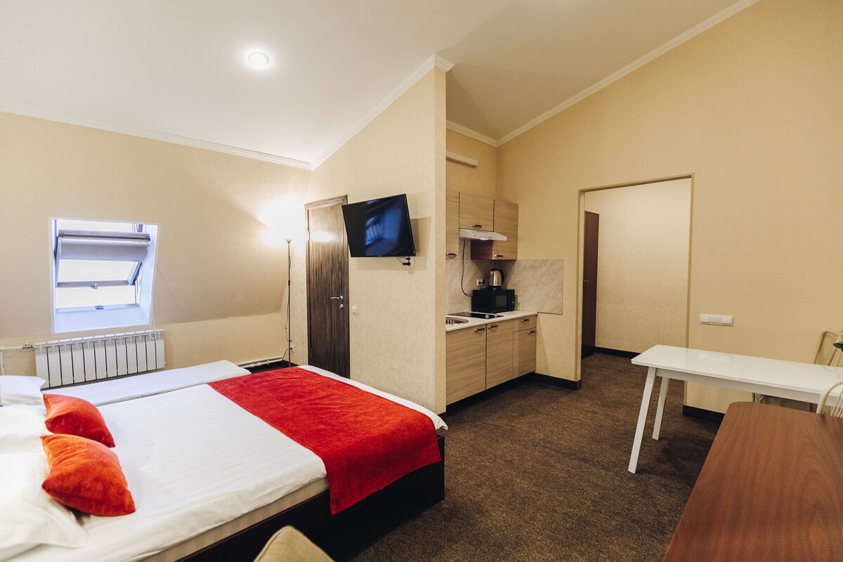 A hotel room with a bed, a desk, a TV, a microwave, and a kitchenette.