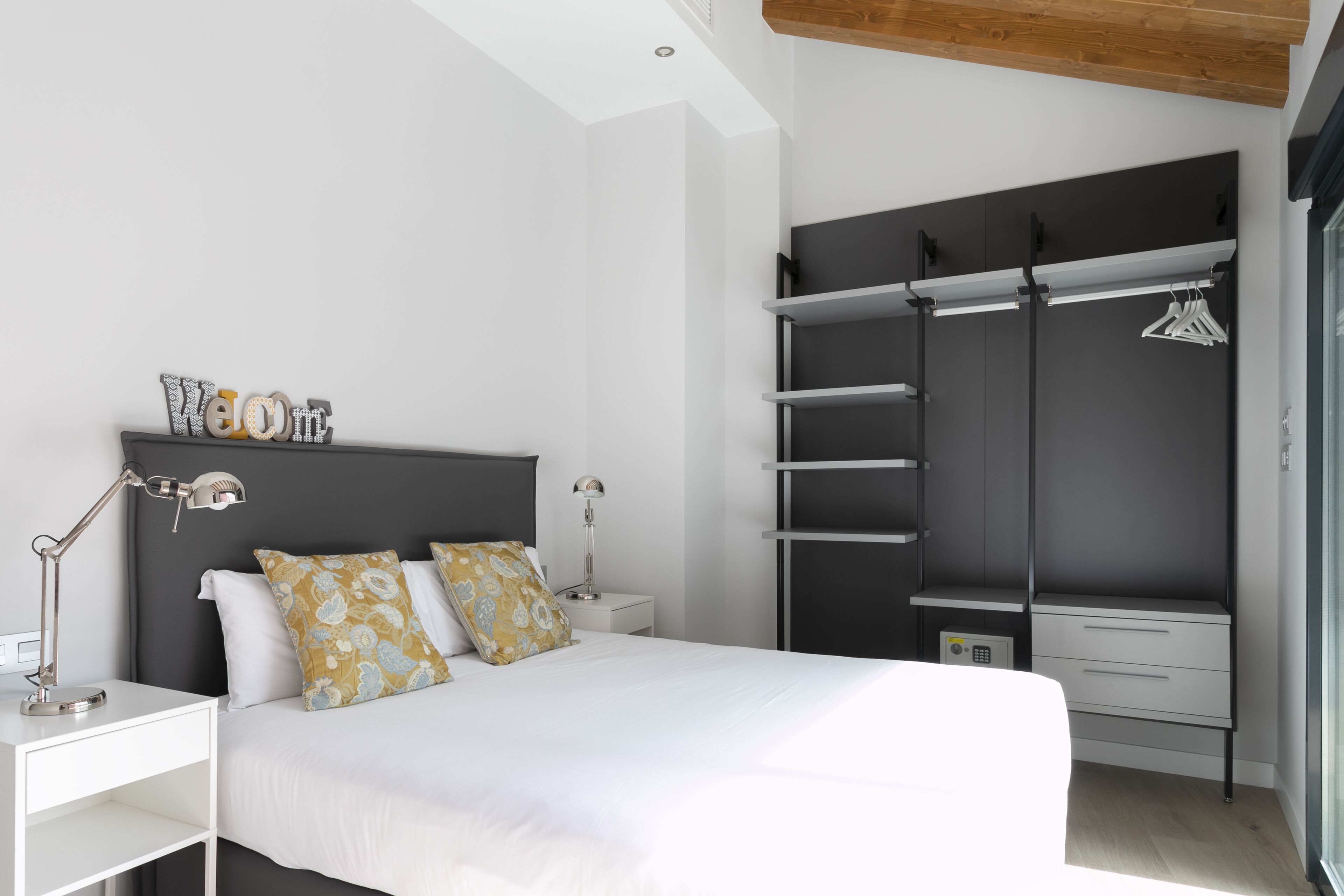 A modern bedroom with a bed, bedside tables, a wardrobe, and a hanging clothes rack.