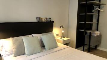 Un lit bien fait, avec des oreillers, une lampe de chevet et une petite table de chevet sur laquelle se trouve une serviette pliée et un téléphone.