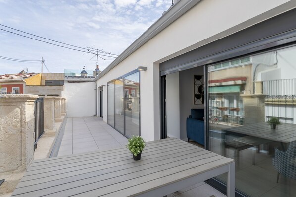 Un balcón moderno al aire libre con una mesa de madera y una planta en maceta.