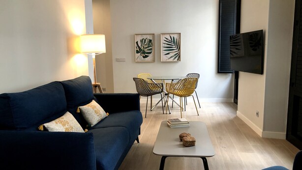 Uma sala de estar moderna com um sofá azul escuro, uma mesinha de centro e um espaço de jantar com uma mesa e cadeiras.
