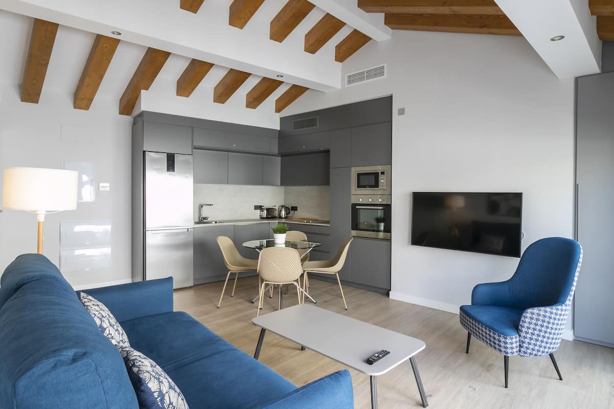 A modern living room with a blue sofa, a patterned armchair, a small table, and a TV mounted on the wall.