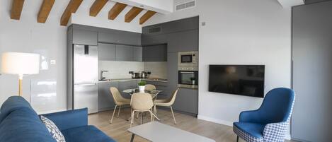 Una sala de estar moderna con un sofá azul, un sillón estampado, una mesita y un televisor montado en la pared.