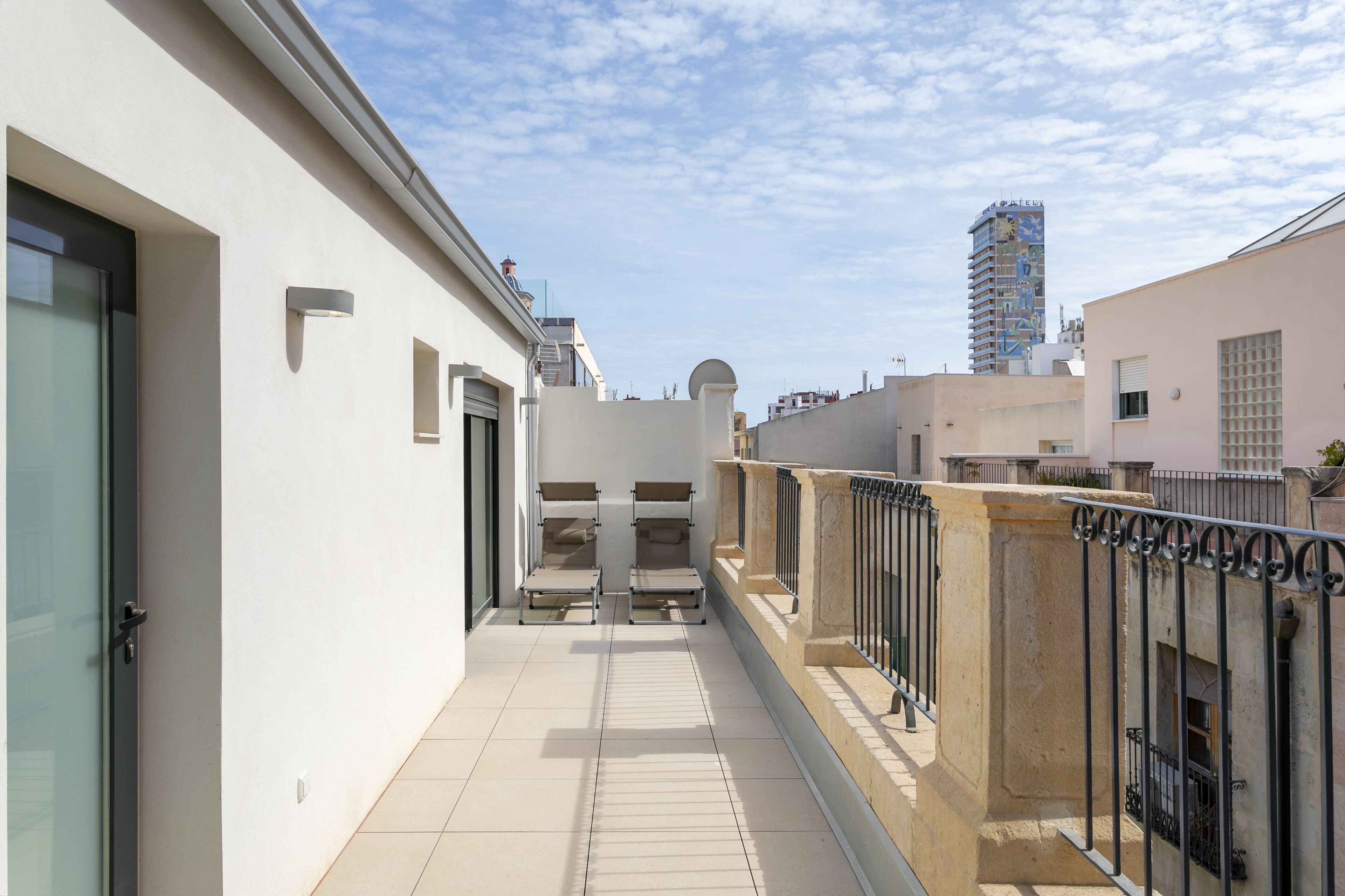 A narrow balcony with a metal railing, a door on the left, and a building in the background.