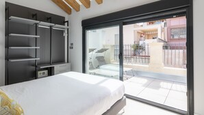 Um quarto com uma cama, um guarda-roupa, uma escrivaninha e uma porta de vidro deslizante que dá para uma varanda.