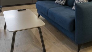 Uma sala de estar moderna com um sofá azul, uma poltrona estampada e uma pequena mesa branca.