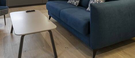 A modern living room with a blue sofa, a patterned armchair, and a small white table.