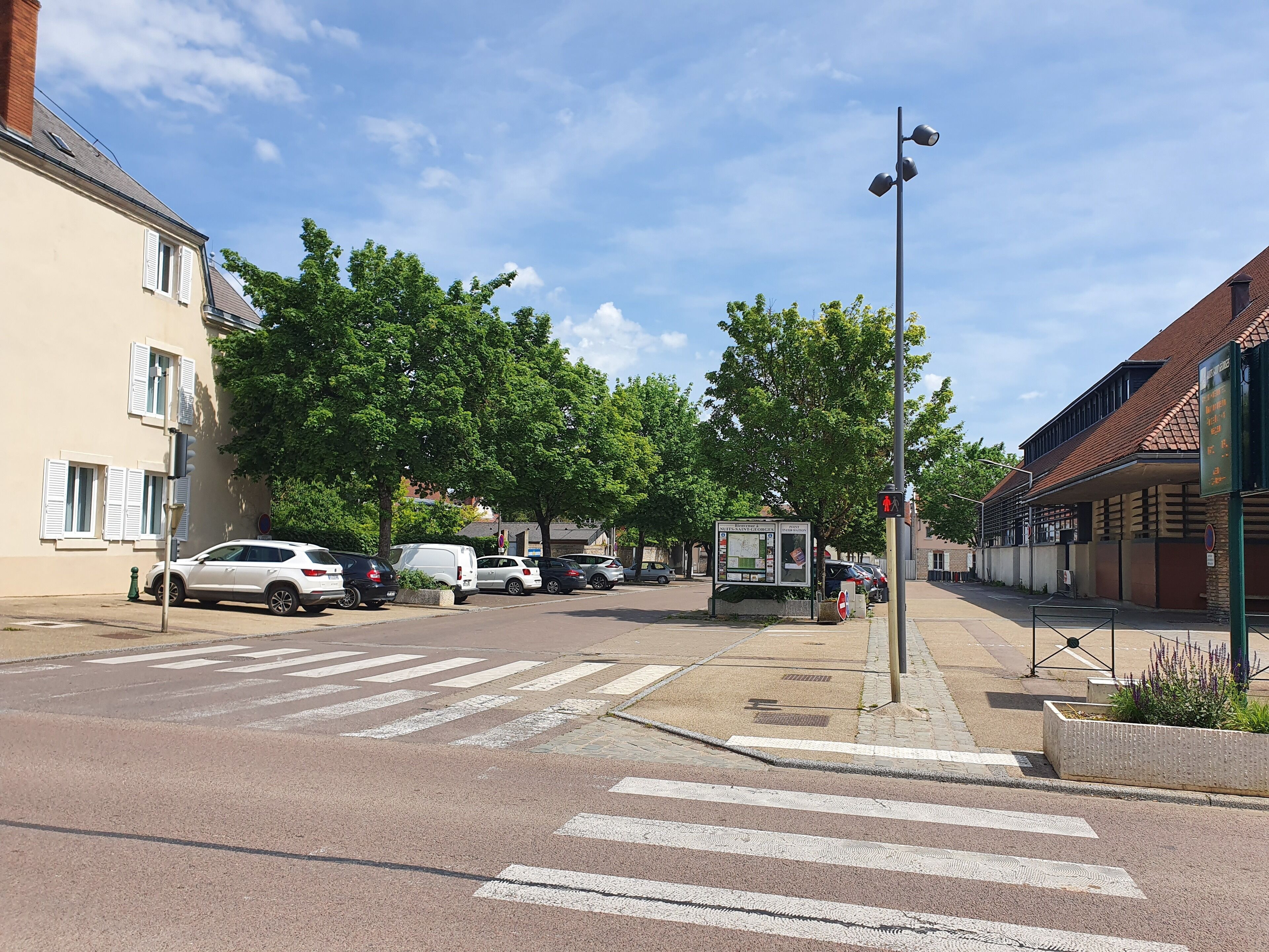 Eine Straße mit parkenden Autos, einem Fußgängerüberweg und einem Gebäude mit einer Schautafel.