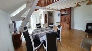 A dining area with a table set for four, a staircase leading to an upper level, and a kitchen visible in the background. - Apartment 37 m² Nuits Saint Georges (Nuits-Saint-Georges)