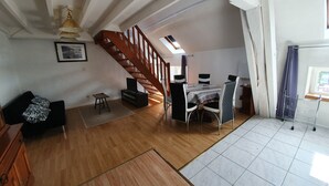 A spacious loft with a wooden staircase, a dining area with a table and chairs, a black sofa, a small TV, and a ceiling fan. - Apartment 37 m² Nuits Saint Georges (Nuits-Saint-Georges)