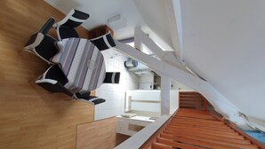 A modern interior with a wooden floor, a staircase with orange railings, and a dining area with striped chairs and a white table. - Apartment 37 m² Nuits Saint Georges (Nuits-Saint-Georges)