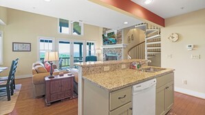 A kitchen with a granite countertop, a dishwasher, and a built-in stove. There is a dining area with a table and chairs, and a staircase leading to an upper level. - Wintergreens R1231-Mtn Condo/View, Gated Resort, Indoor/Outdoor Pools & Hot Tub (Banner Elk)