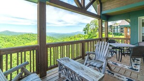 A wooden deck with a view of green mountains, a table with chairs, and a covered area with a view. - Wintergreens R1231-Mtn Condo/View, Gated Resort, Indoor/Outdoor Pools & Hot Tub (Banner Elk)