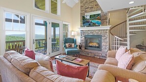 A spacious living room with a fireplace, comfortable seating, a staircase, and a balcony with a view. - Wintergreens R1231-Mtn Condo/View, Gated Resort, Indoor/Outdoor Pools & Hot Tub (Banner Elk)