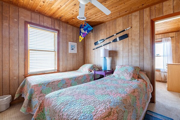 A cabin-style room with two beds, wooden walls, a ceiling fan, and a window with blinds. - Beach Baby - Kitty Hawk MP 2.5, Oceanfront, 3 Bedrooms, Best Views on the OBX, Pets OK (Kitty Hawk)