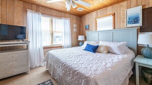 A bedroom with a bed, a television, a ceiling fan, and wooden walls. - Beach Baby - Kitty Hawk MP 2.5, Oceanfront, 3 Bedrooms, Best Views on the OBX, Pets OK (Kitty Hawk)