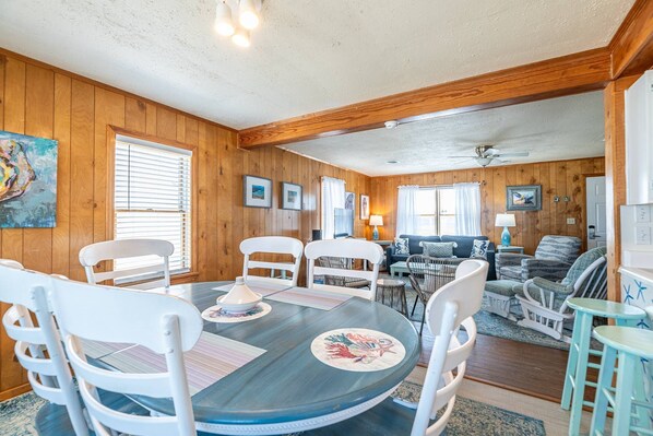 A cozy room with a dining table, chairs, a sofa, and a ceiling fan. - Beach Baby - Kitty Hawk MP 2.5, Oceanfront, 3 Bedrooms, Best Views on the OBX, Pets OK (Kitty Hawk)