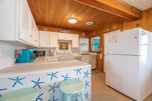 A kitchen with wooden cabinets, a white refrigerator, and a blue coffee maker. - Beach Baby - Kitty Hawk MP 2.5, Oceanfront, 3 Bedrooms, Best Views on the OBX, Pets OK (Kitty Hawk)