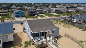 A beachfront house with a deck and outdoor seating area, surrounded by a sandy beach and a residential neighborhood. - Beach Baby - Kitty Hawk MP 2.5, Oceanfront, 3 Bedrooms, Best Views on the OBX, Pets OK (Kitty Hawk)