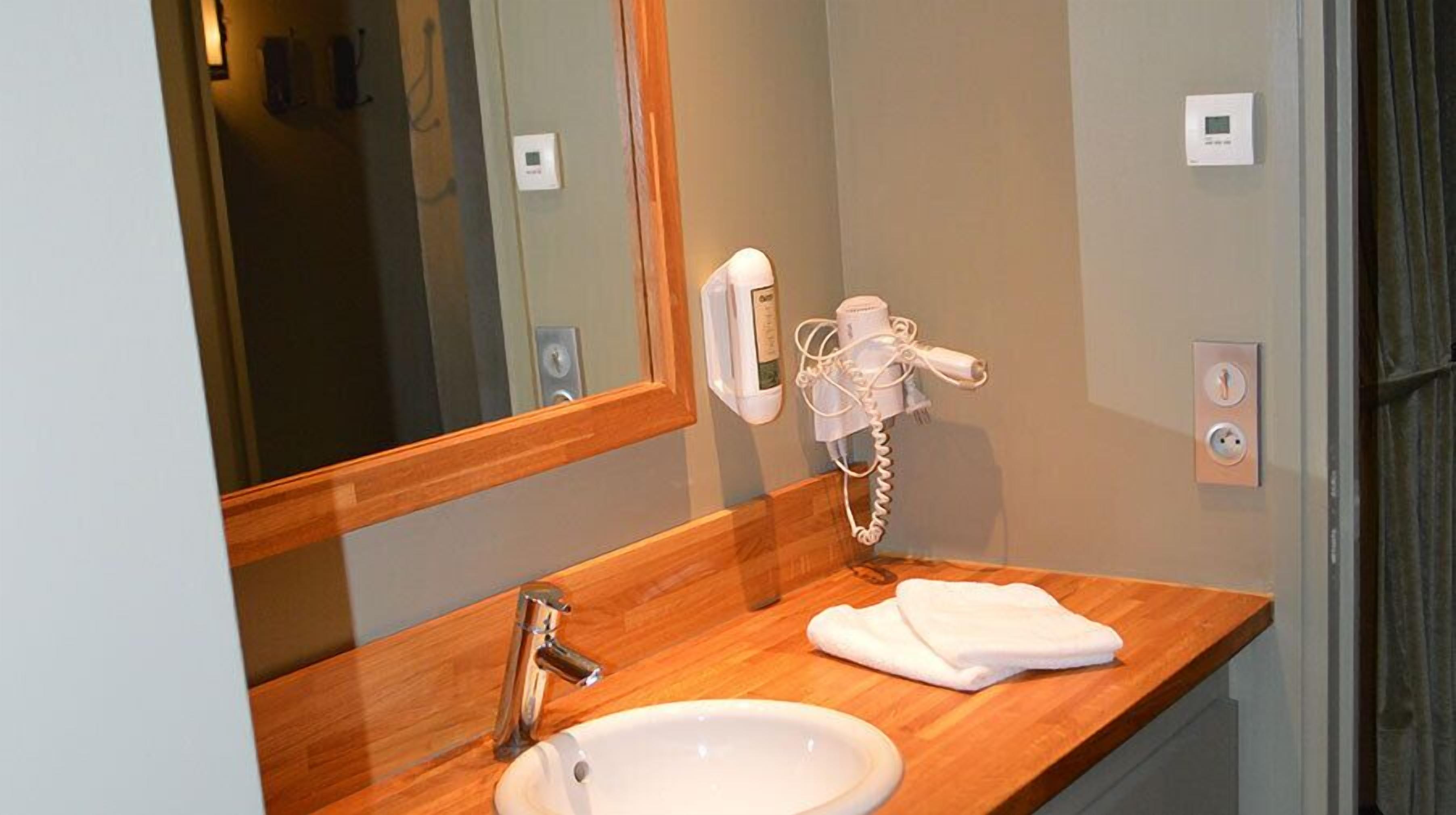 A bathroom with a wooden vanity, a white sink, a mirror, a hairdryer, and a towel.
