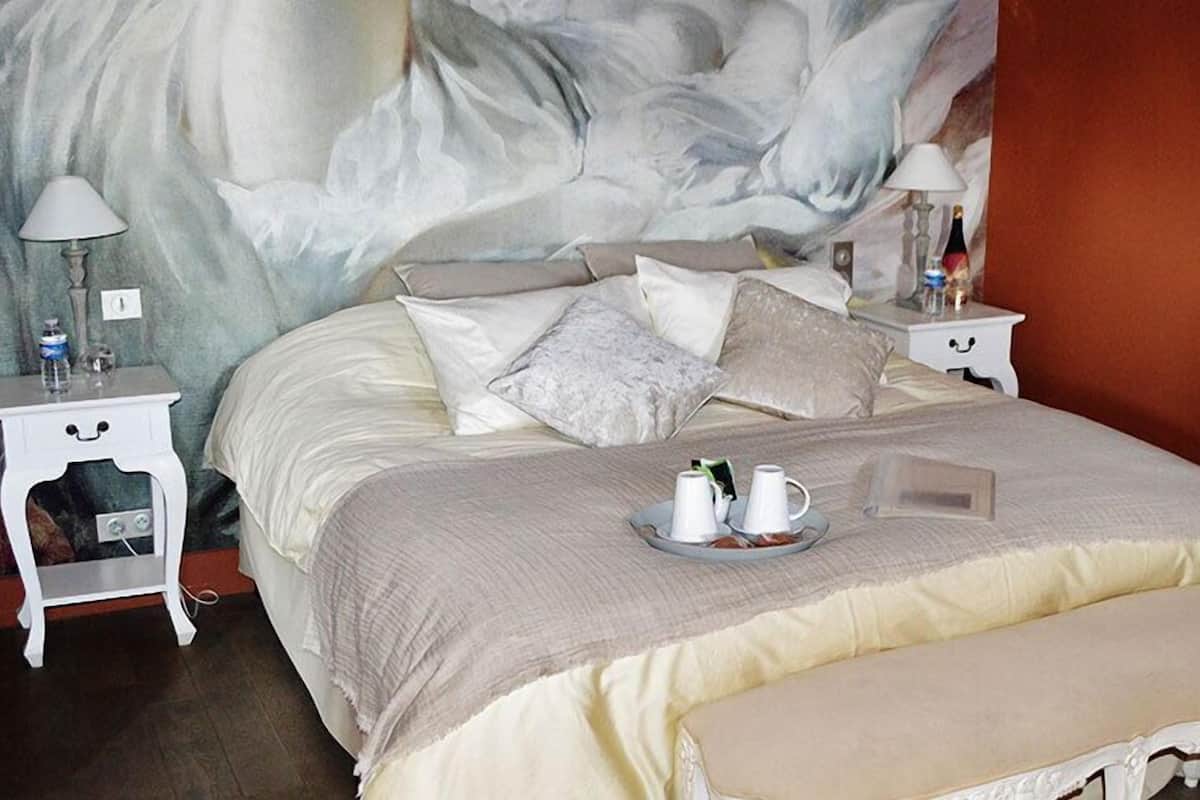 A neatly made bed with a tray of cups and a teapot, two bedside tables with lamps, and a large abstract painting on the wall.