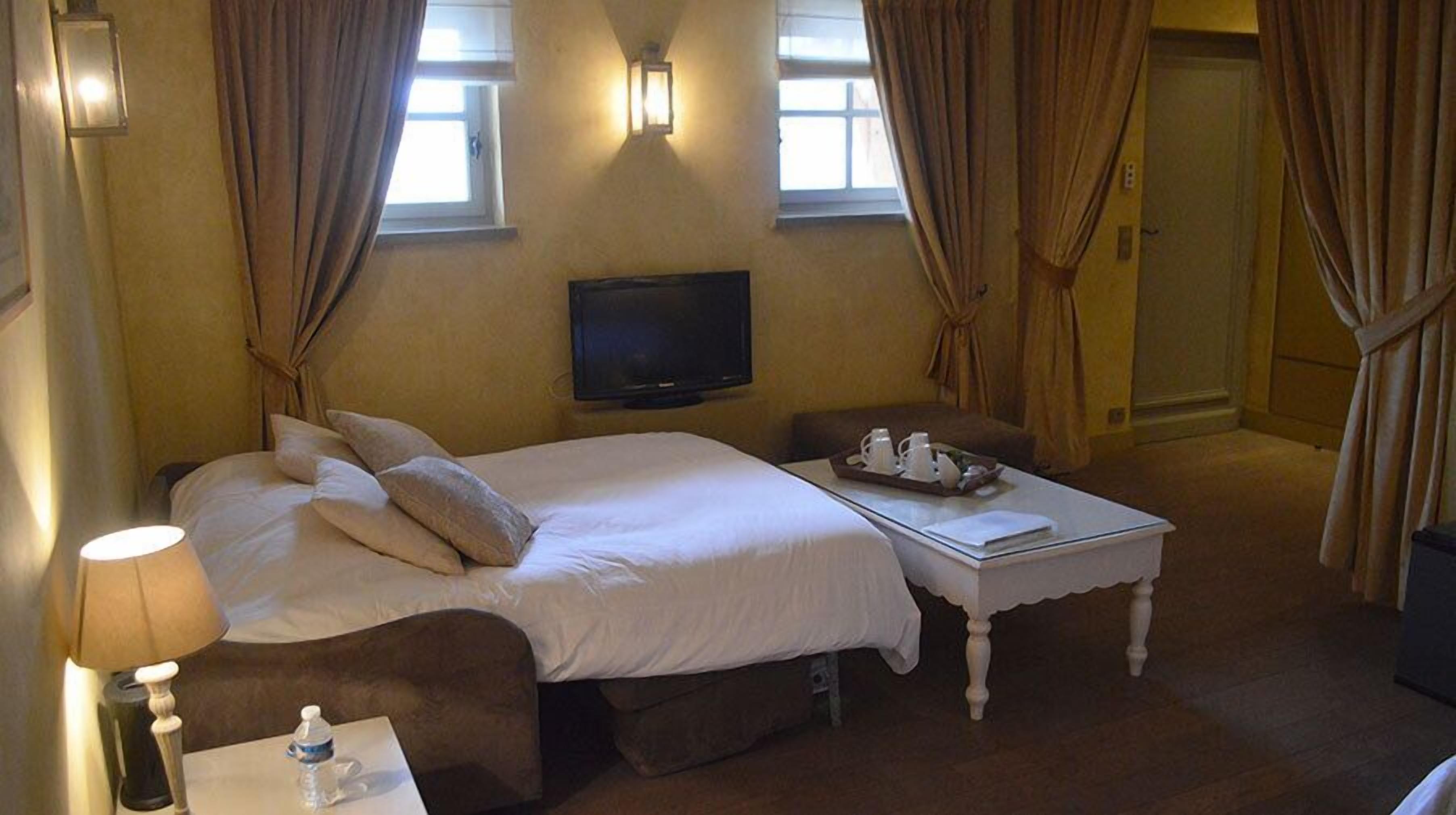 A hotel room with a bed, a TV, a bedside table with a tray of items, and a chair.