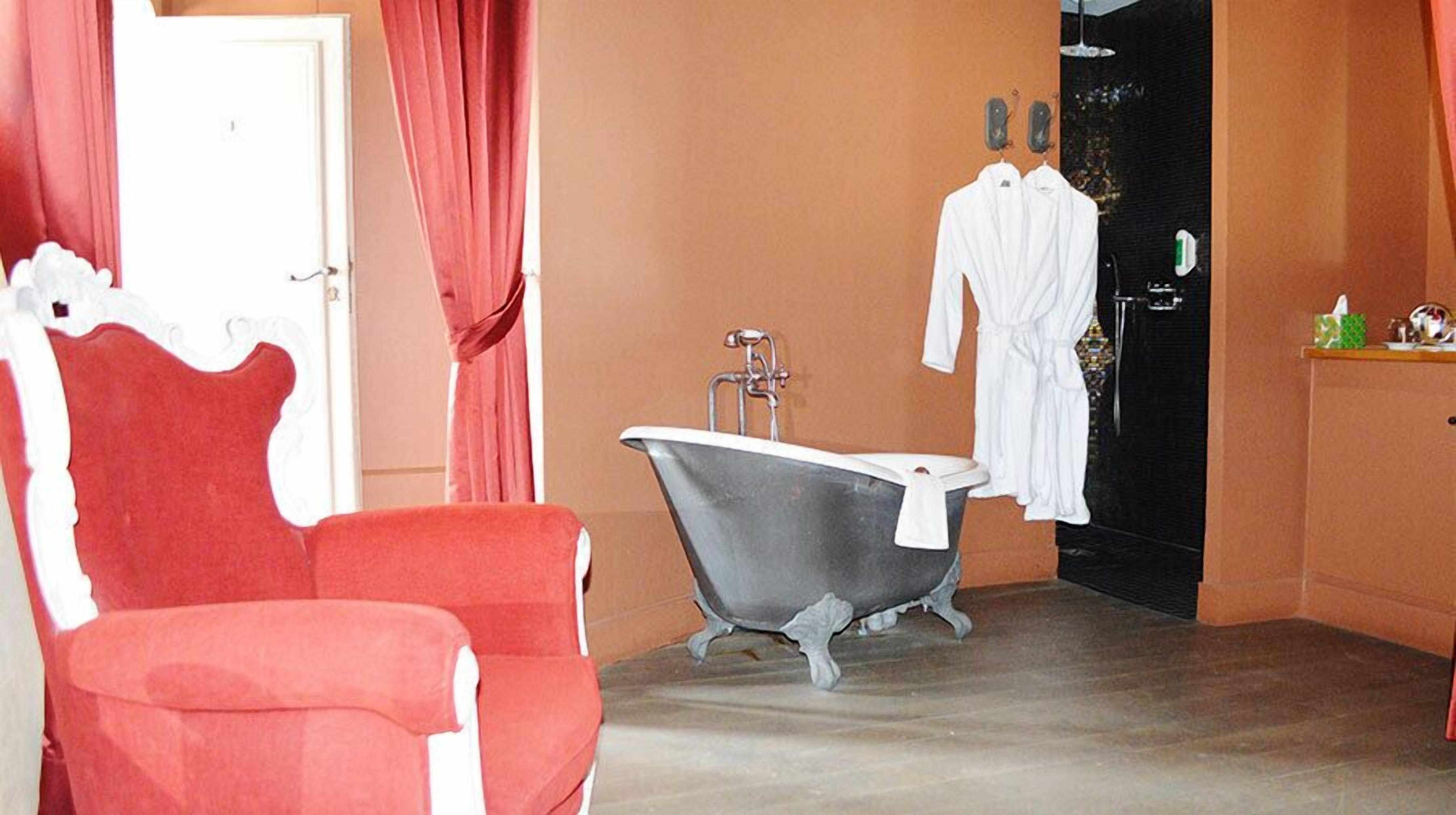 Une salle de bain avec une baignoire sur pieds, une chaise rouge et deux peignoirs blancs accrochés au mur.