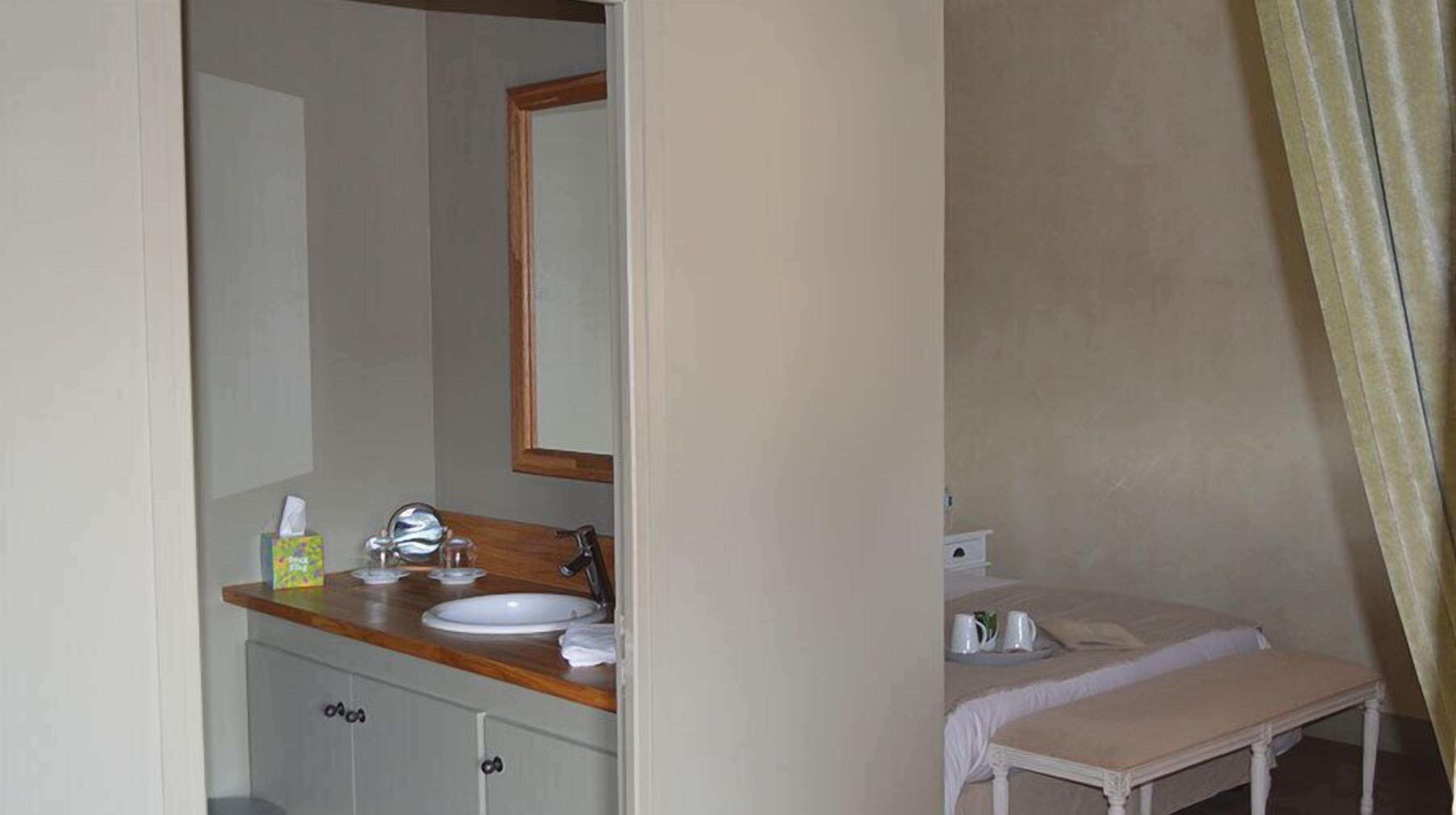 Une salle de bain avec un meuble-lavabo en bois, un miroir, un évier et une table de chevet avec un lit.