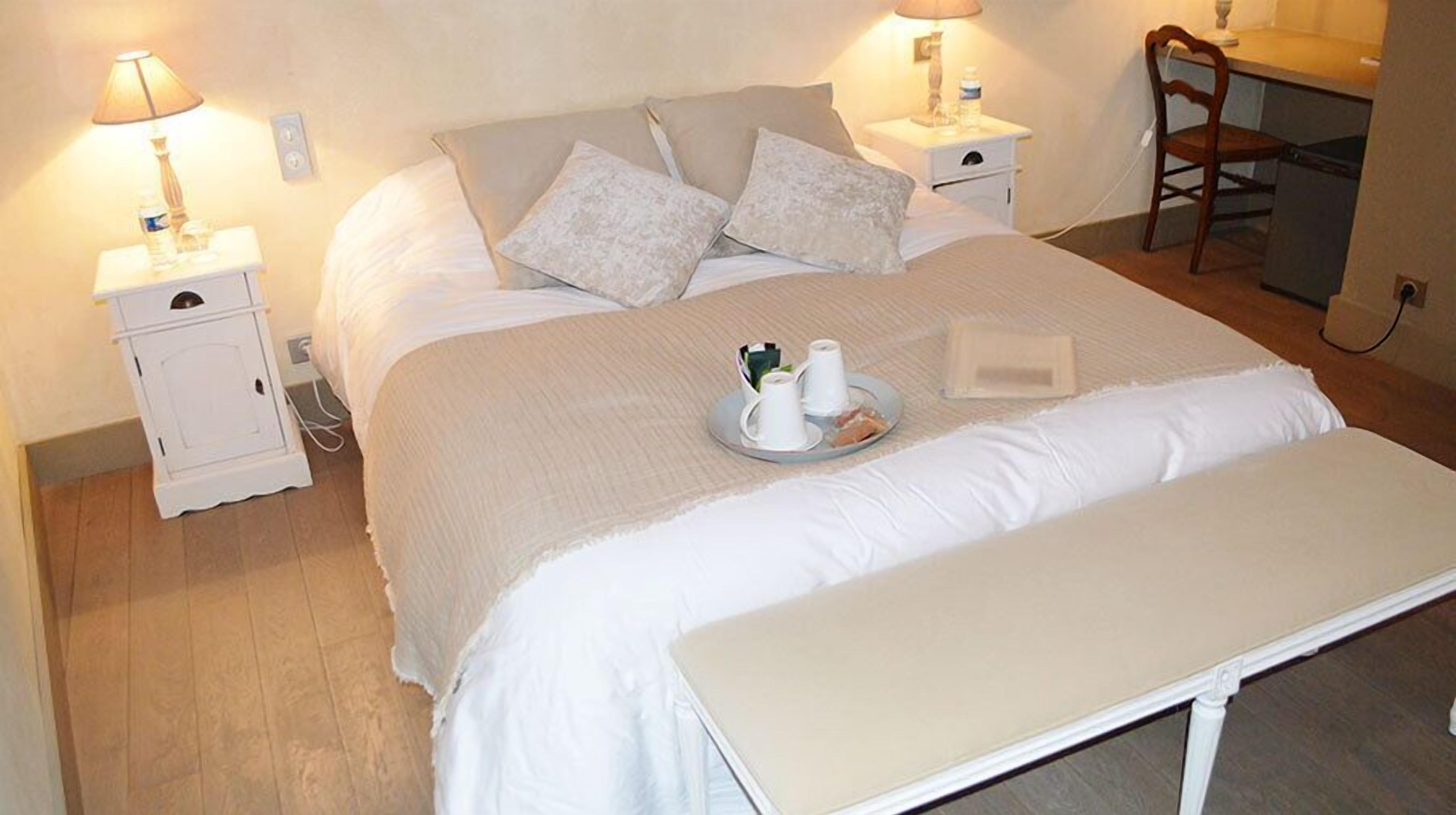 A neatly made bed with a tray of breakfast items, two bedside tables with lamps, and a chair in a room with wooden flooring.