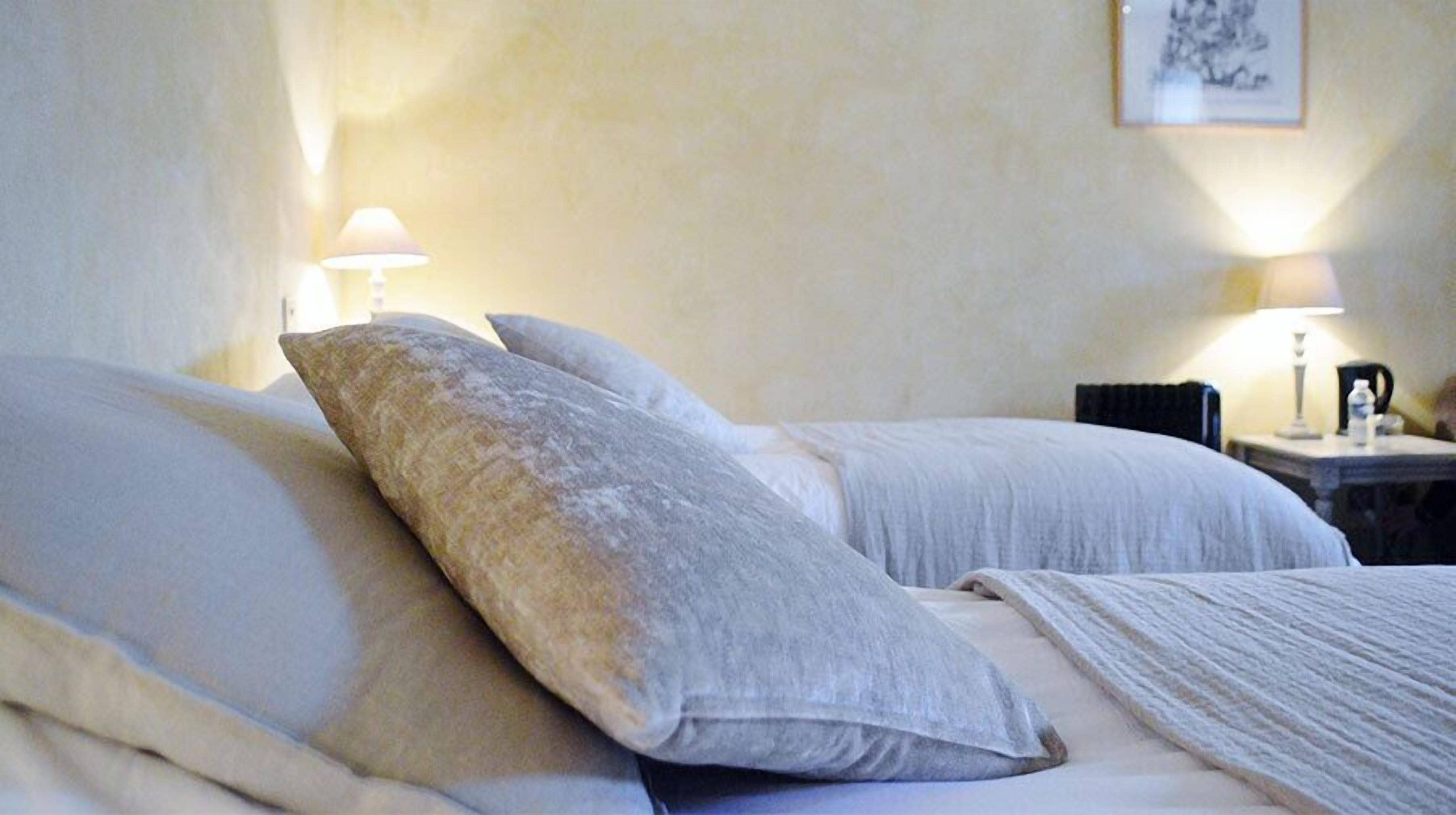 A hotel room with two beds, each with white linens and pillows. There are two bedside tables with lamps and a framed picture on the wall.