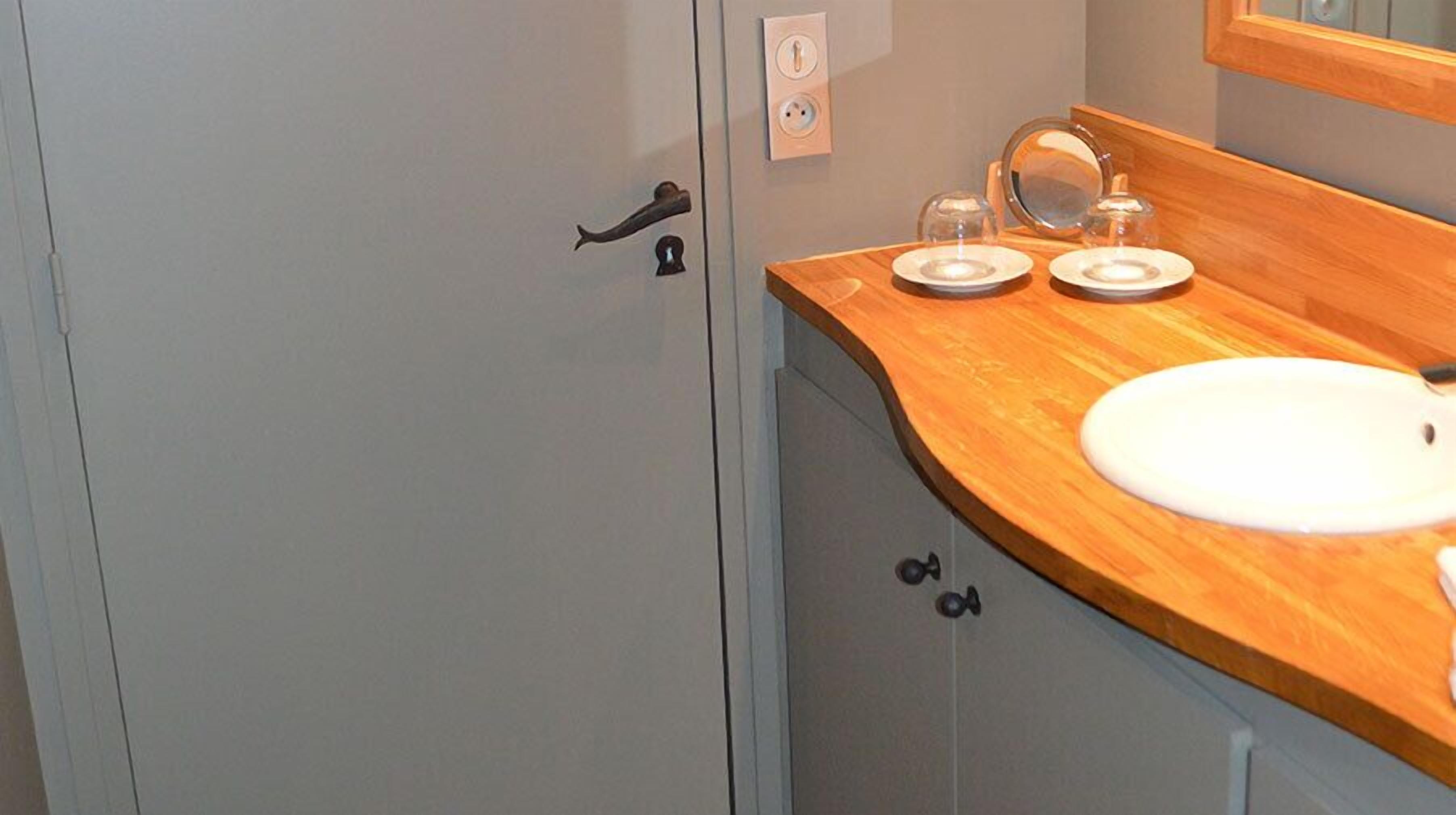 Un baño con puerta gris, encimera de madera, lavabo blanco y espejo sobre el lavabo.
