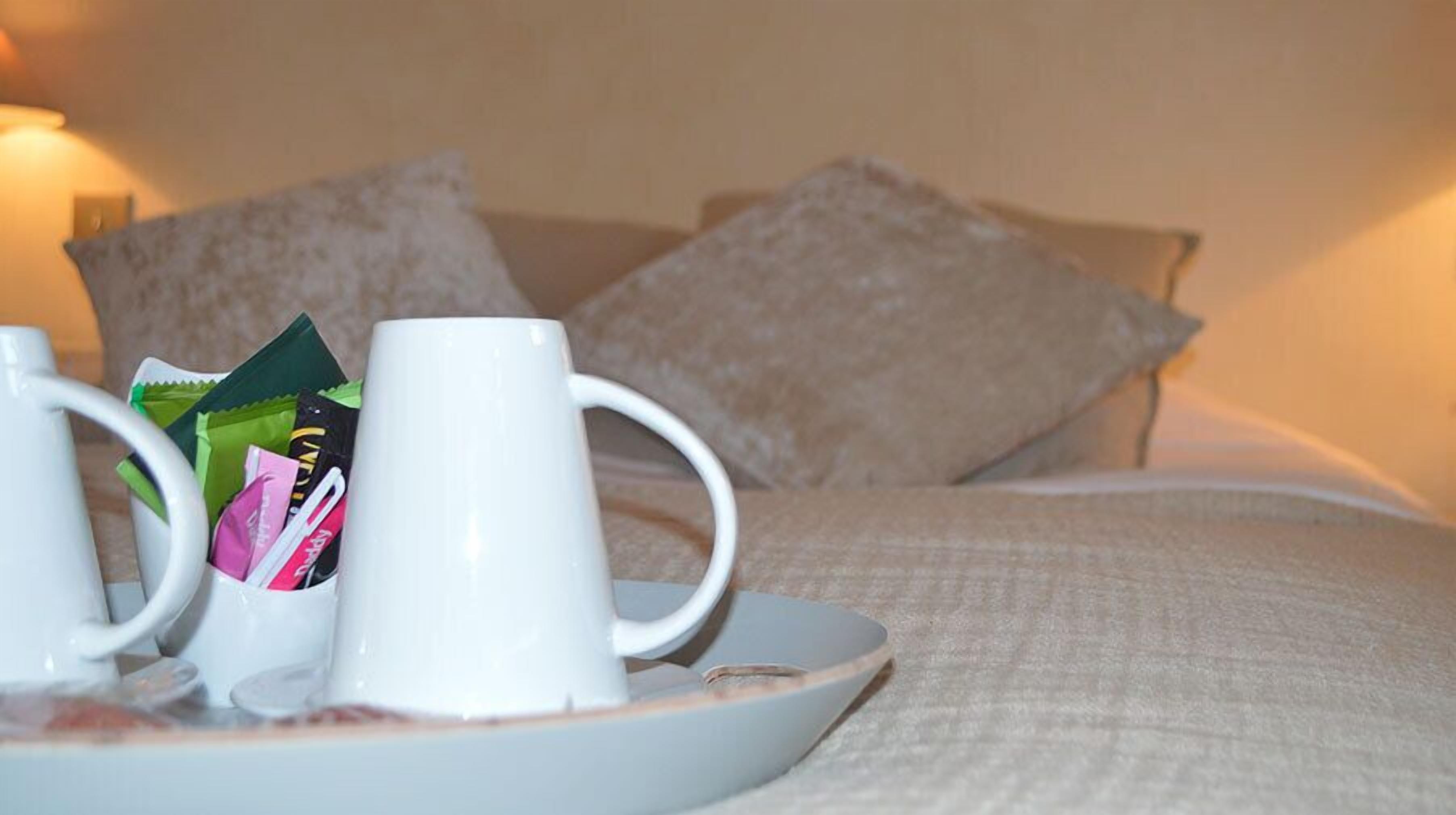 Una cama con almohadas y una bandeja con una taza y refrigerios.