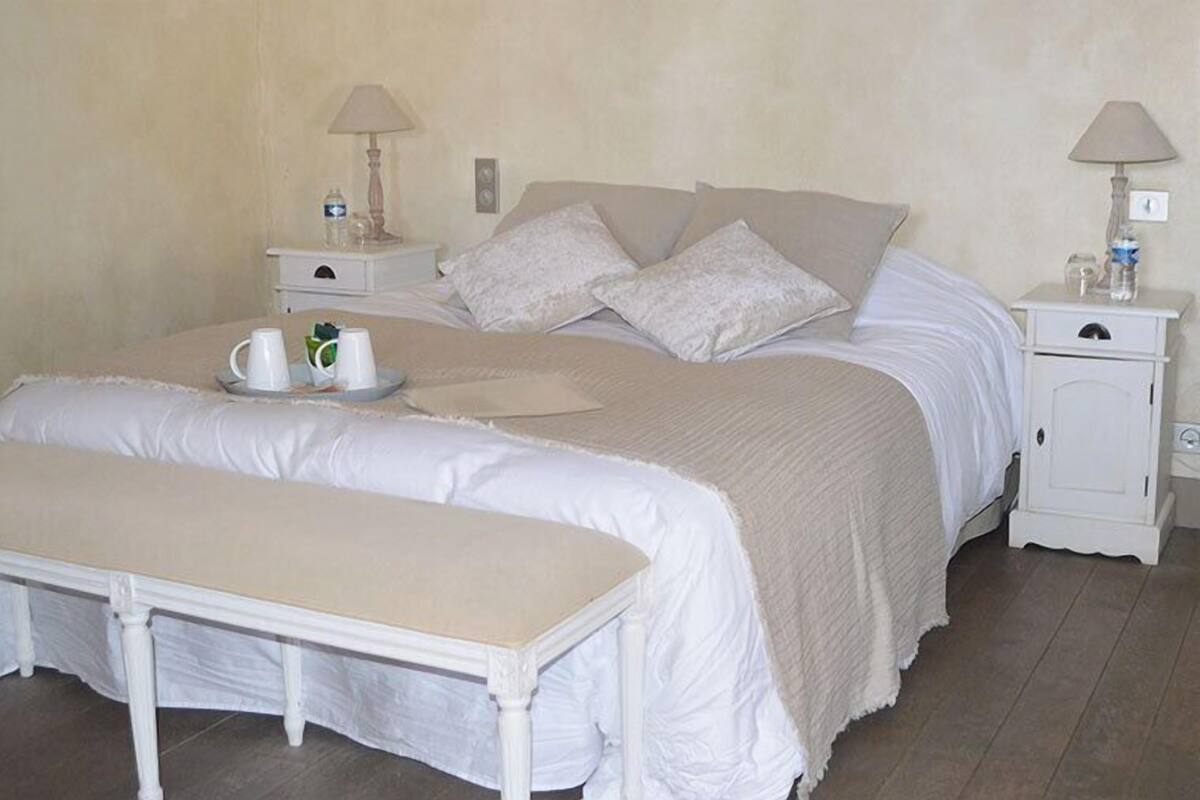 A bedroom with a bed, bedside tables, a bench, and a lamp.