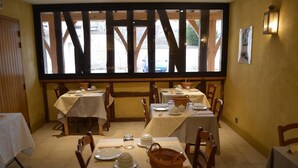 A dining area with tables set for service, a large window with wooden beams, and a view of the outside. - Le Clos Margot (Blancs-Coteaux)