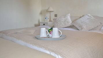 A neatly made bed with a tray of two white mugs and a small box of tissues.