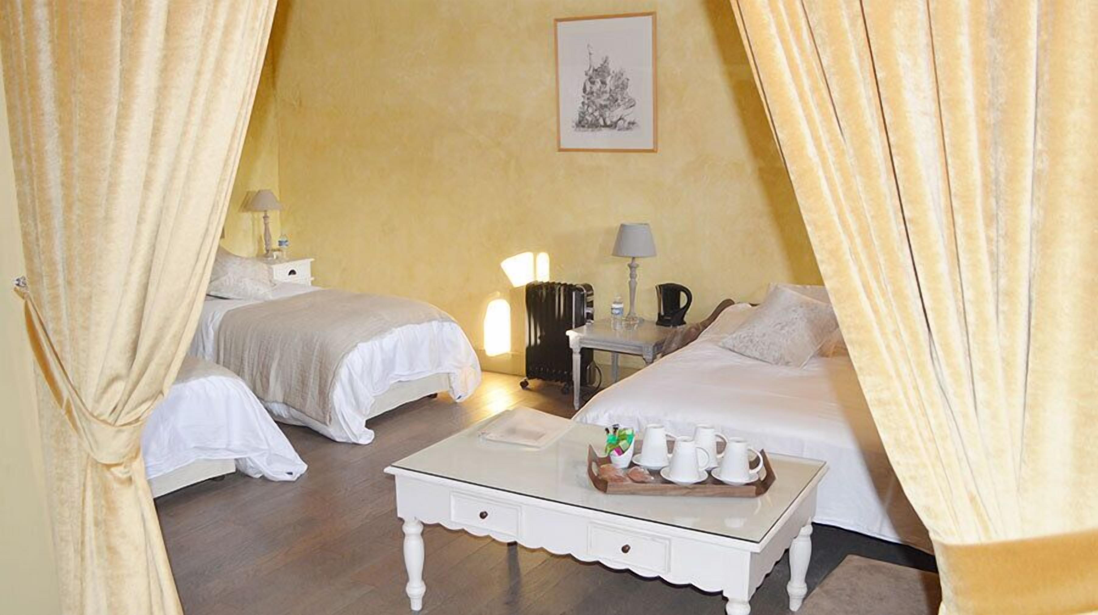 A hotel room with two beds, a small table with a tray of cups and a bottle, and a lamp on a nightstand.