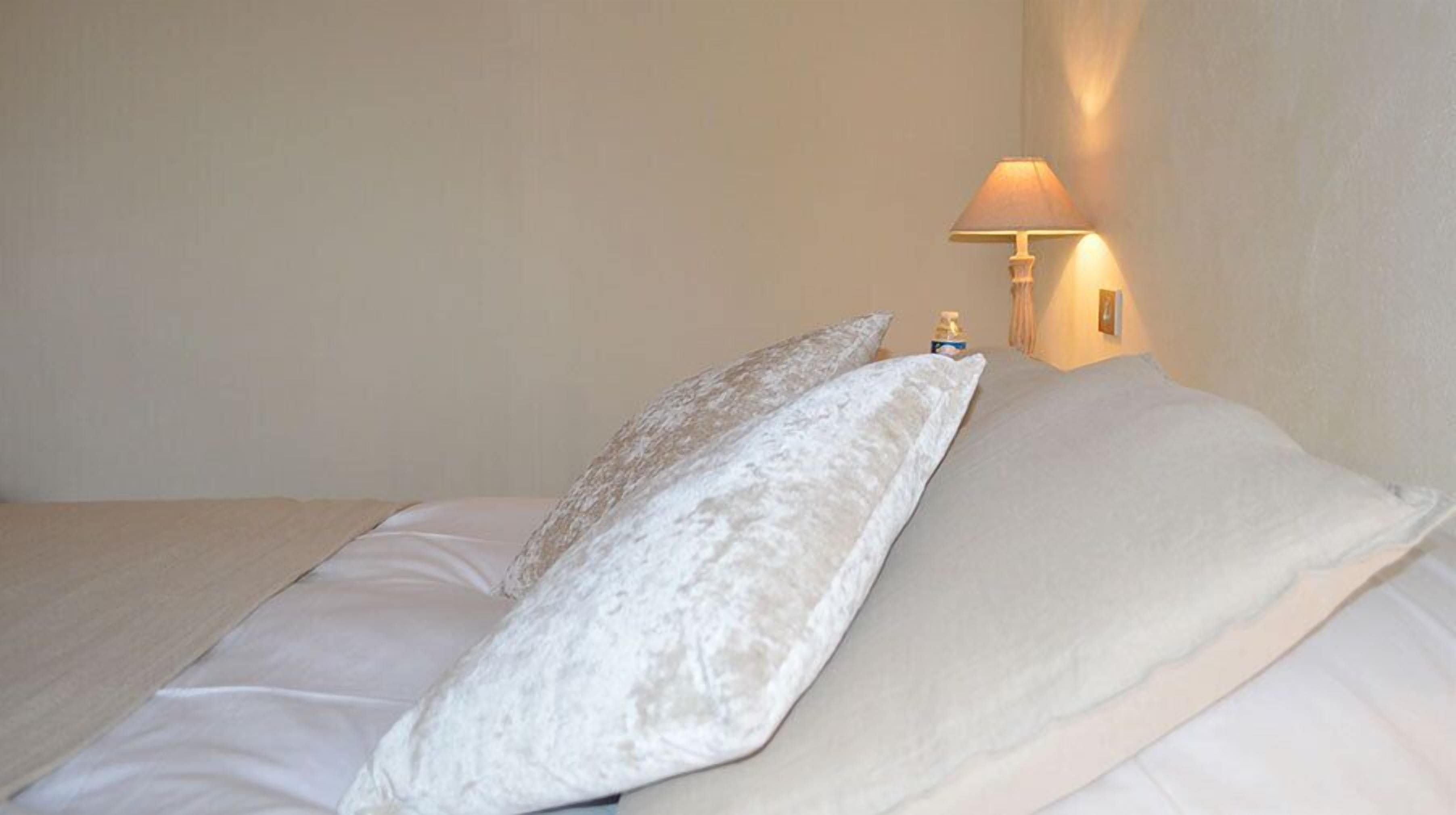 Un lit avec deux oreillers et une lampe fixée au mur.