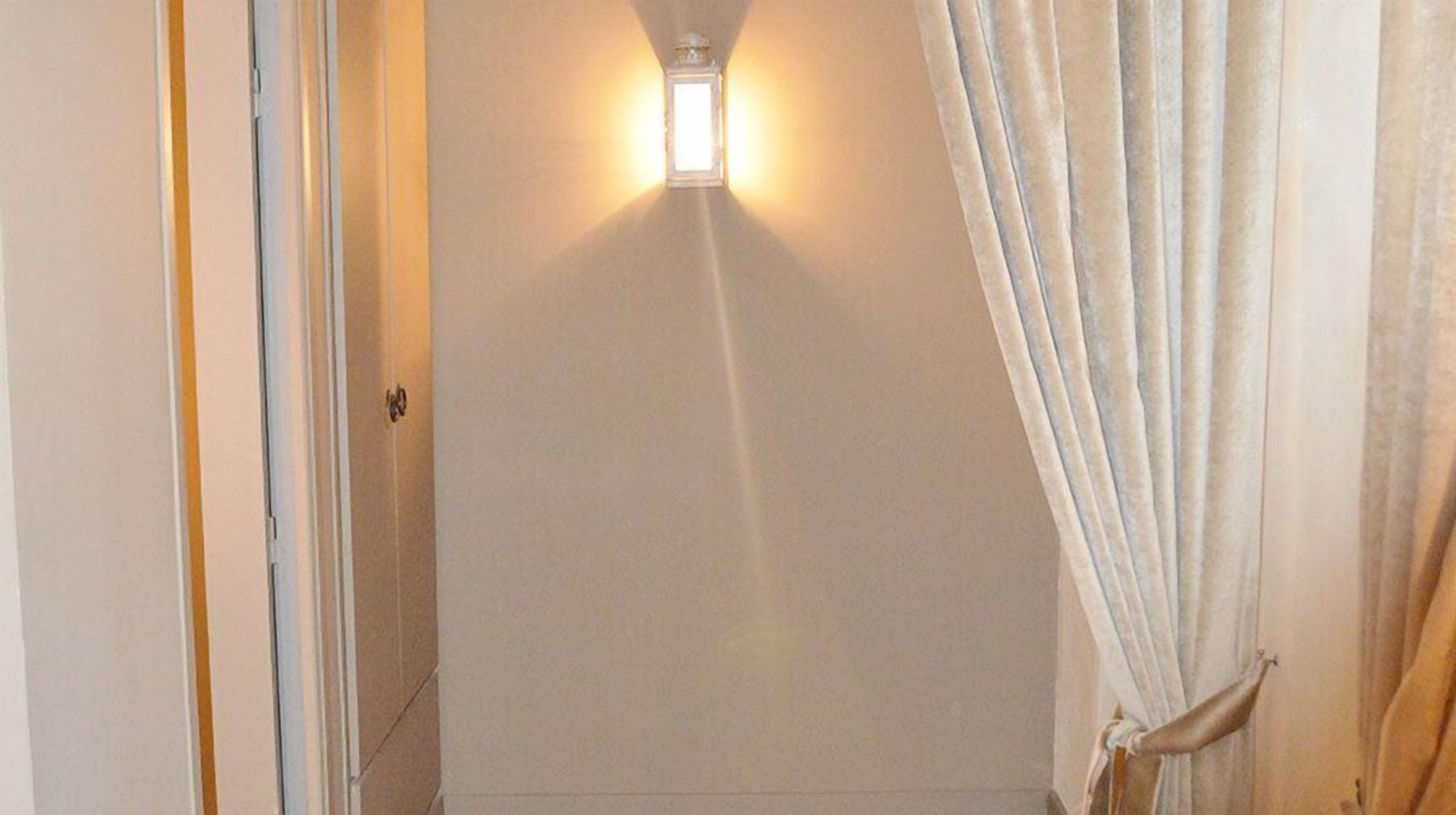 A narrow hallway with a light fixture on the wall, a door on the left, and a curtain on the right.