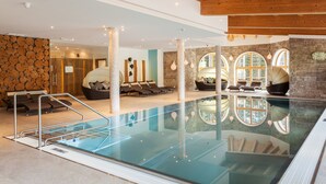 An indoor swimming pool with lounge chairs and a stone wall.