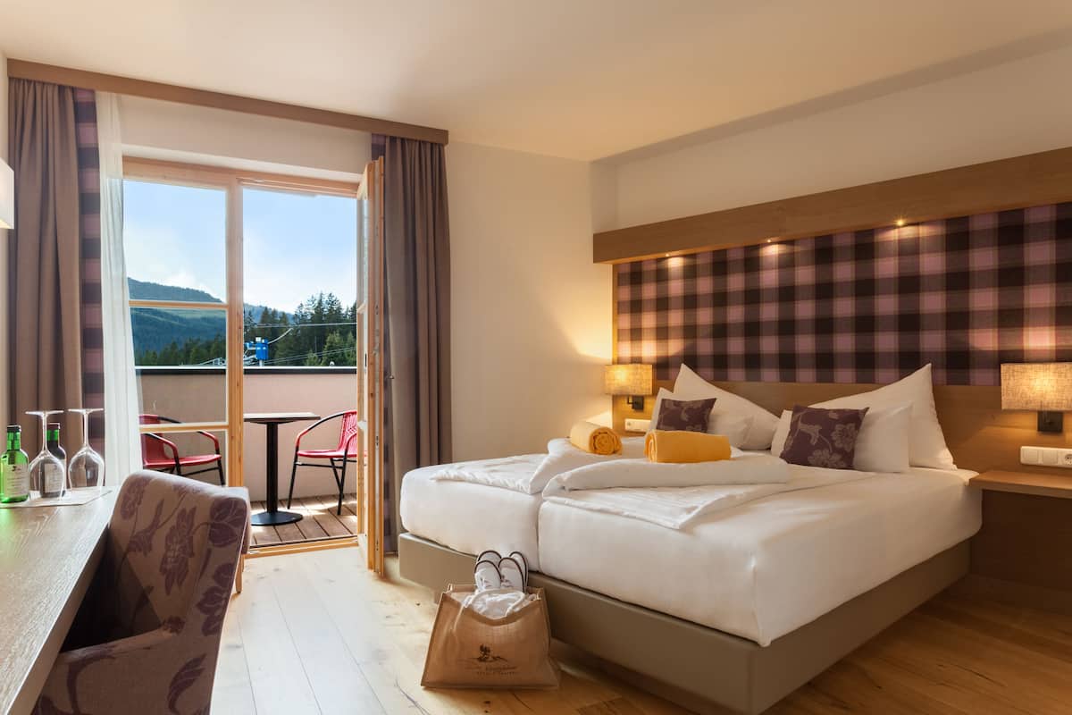 Ein Hotelzimmer mit Bett, Tisch mit Stühlen, Blick ins Freie und einer Rezeption.