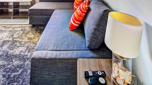 Un salon moderne avec un canapé gris, une table en verre surmontée d’une lampe, et des œuvres d’art représentant la Tour Eiffel et un paysage urbain.