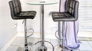 Une chambre moderne dotée d’un téléviseur à écran plat fixé au mur, de deux tabourets de bar, d’une petite table ronde et d’une fenêtre avec un rideau.