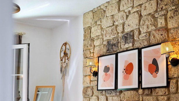 A bedroom with a stone wall, a bed with patterned bedding, and wall-mounted artwork. - Alacati Lulja Hotel (Cesme)