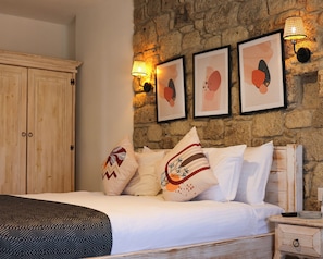 A bedroom with a stone wall, a wooden wardrobe, and a bed with patterned pillows. - Alacati Lulja Hotel (Cesme)