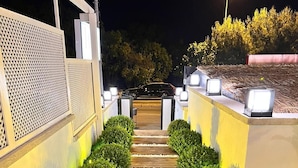 A wooden pathway flanked by trimmed hedges and illuminated by ground lights, leading to a vehicle parked at the end. - Alacati Lulja Hotel (Cesme)